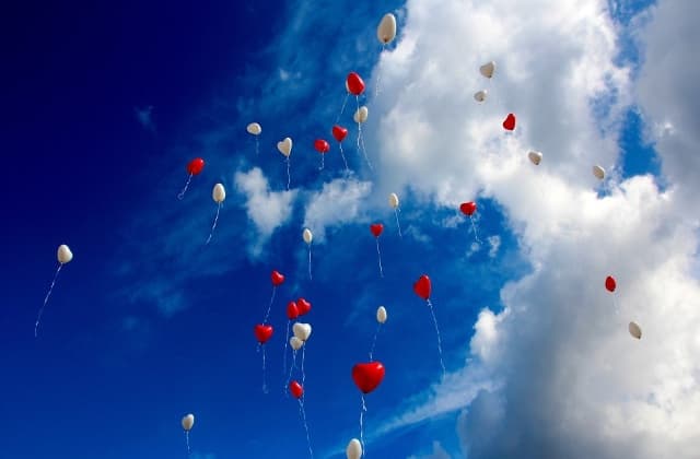 ballons blancs et rouges en forme de coeurs lachés dans un ciel bleu nuageux
